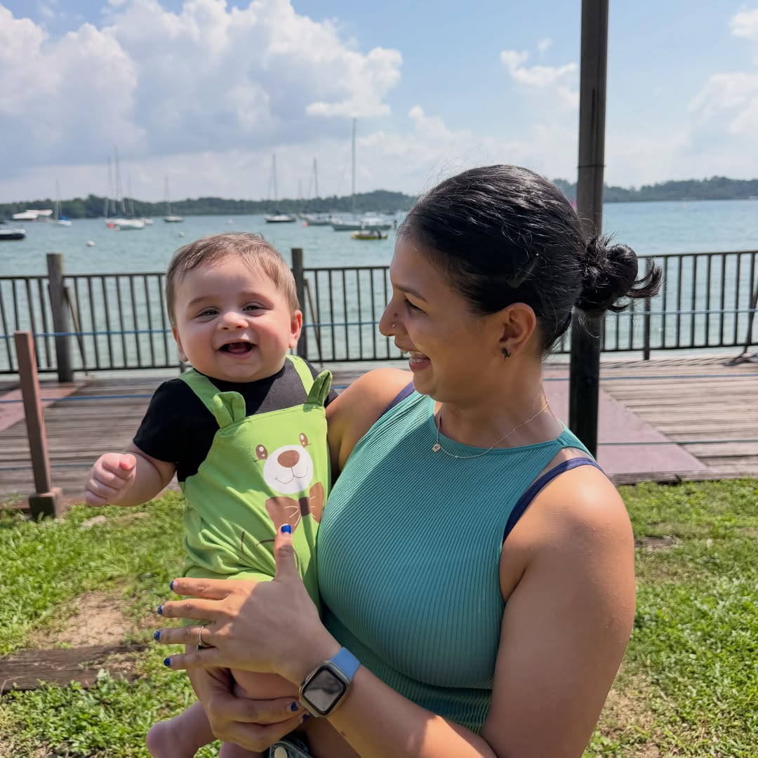 Ankita Pandey by the waterfront, smiling and holding her baby
